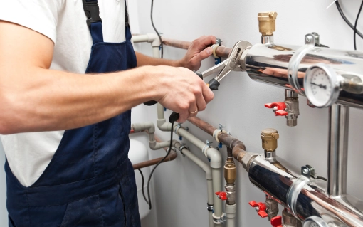 Hydraulik w niebieskim kombinezonie dokręca rurę kluczem, pracując przy instalacji wodno-kanalizacyjnej